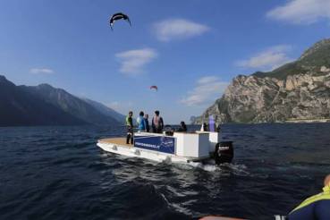 Das Platform Boot des Vereins auf dem See. Die Sonne scheint und im Hintergrund sieht man 2 Kites.