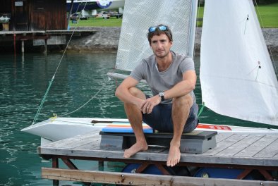 Reini Glanz sitzt auf einem 'Aerobic Stepper' auf einem Steg. Im Hintergrund sieht man ein kleines Segelboot.