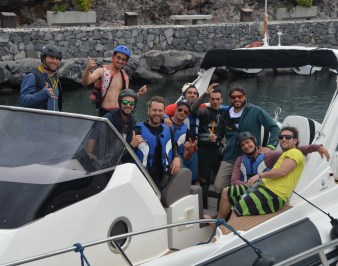 The whole crew in a boat. Some make the hang loose sign with their hands.