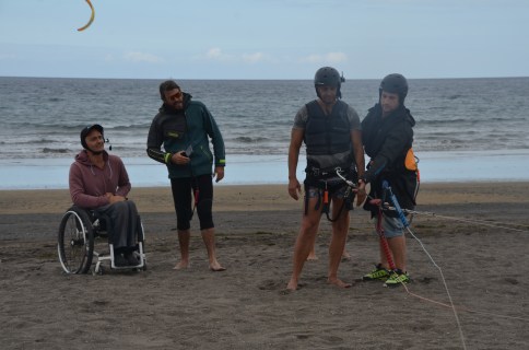 from left to right: wheelchair user with headset, head instructor and the kiteboarding student with helmet and harness and the kite conneted to it. With the student is another instructor - also with helmet.