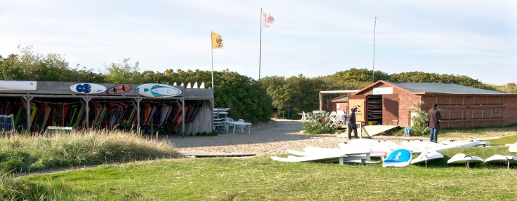 The wooden hut of the school with surfboards in front.