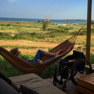 Man lying in a hammock. Next to him a wheelchair. In the background the steppe and the bay.