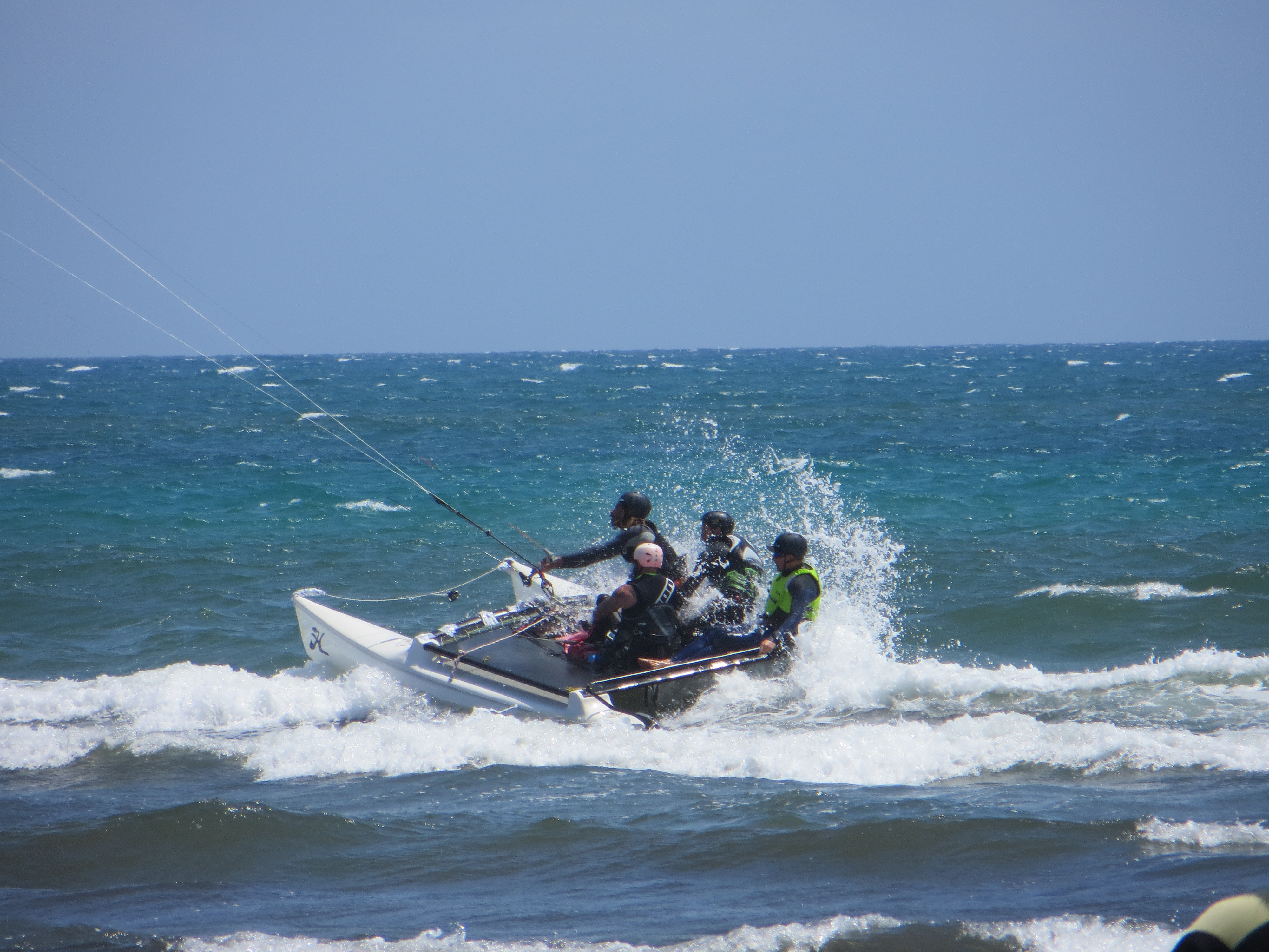 A hobie cat with a kite instead of a sail. 4 people sitting on top. White spray from the speed.