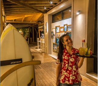 The waitress with a pony tail wearing a red Hawaiian blouse with white flowers. In her hand a tray with some cocktails.