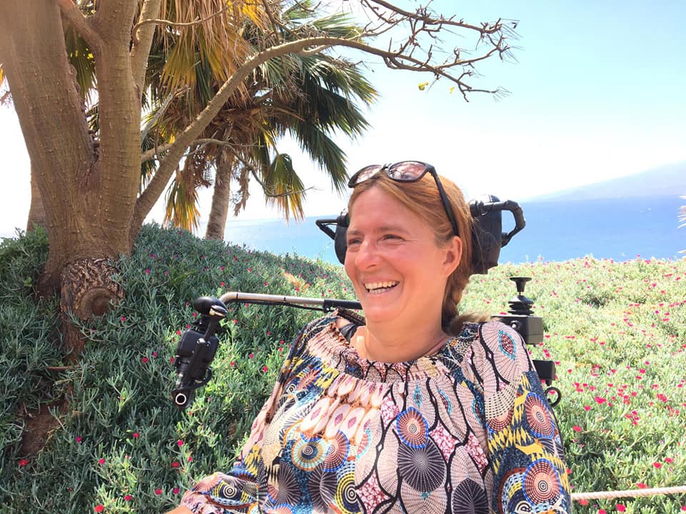 Woman in an electric wheelchair. In the background you green nature and the sea
