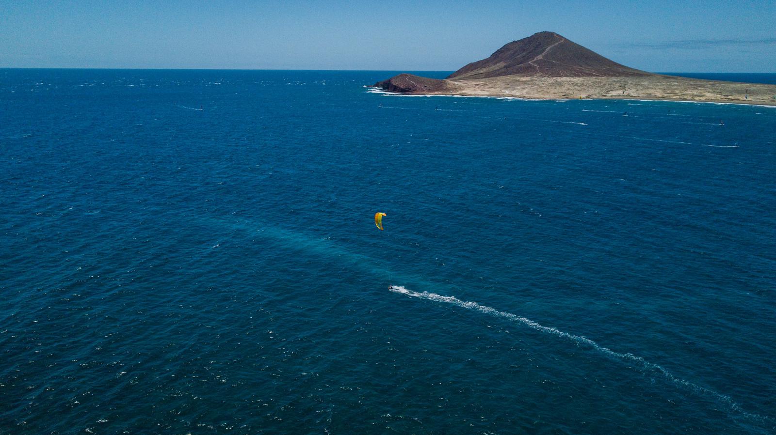 A single yellow kite within a big bay. A small mountain in the background.